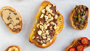 A slice of toast topped with Nutella, fresh banana slices, and a sprinkle of crushed pistachios, presented as a quick and fun snack for kids.